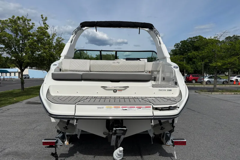Slide: The Image of 2026 Sea Ray SDX 230 boat rear view, parked on pavement under a clear sky. - 4