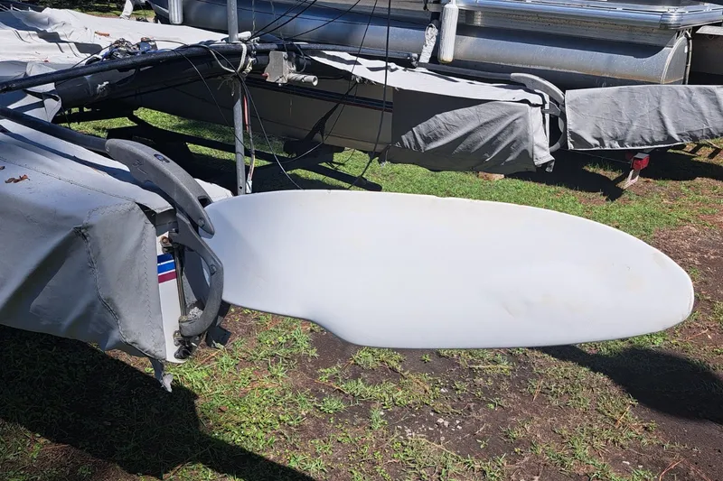 Slide: The Image of 1989 Hobie Cat 21 sailboat with covered hulls and visible rudder on grassy ground. - 4