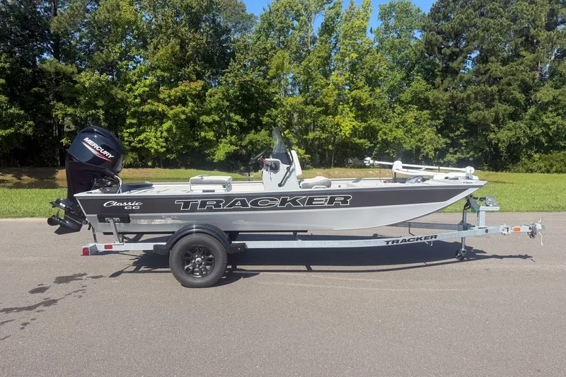The Image of 2027 Tracker Bass Tracker Classic CC boat on trailer, parked on road with green trees background. - 1