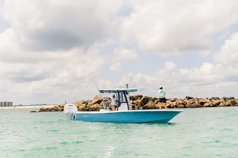 Slide: The Image of 2027 Sea Hunt BX25FS boat on water near rocky shoreline under cloudy sky. - 24