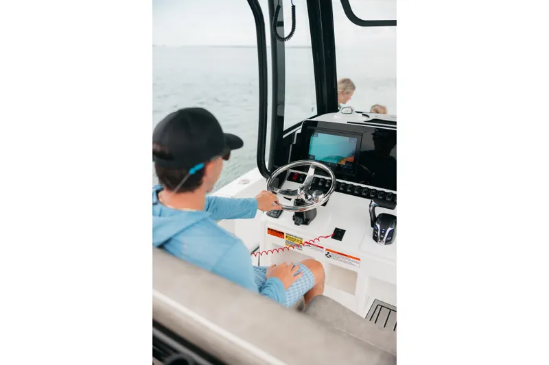 Slide: The Image of Person steering 2027 Sea Hunt BX25FS boat, focusing on navigation controls and display. - 7