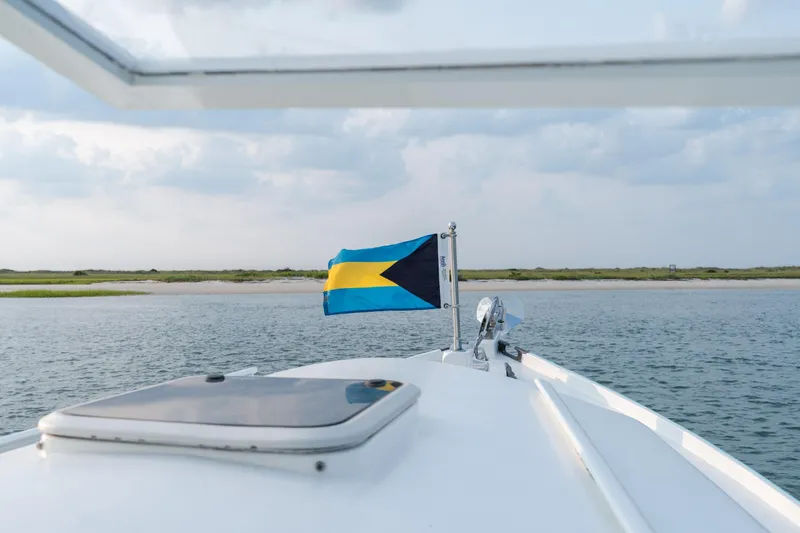 Slide: The Image of Boat with Bahamian flag on water, Albury Brothers, 1958, near sandy shoreline. - 92