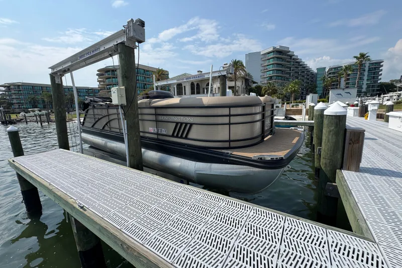 The Image of 2022 Bennington 23 LXFB pontoon boat docked at a marina with modern buildings. - 1
