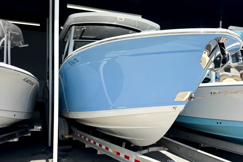 The Image of 2024 Blackfin 272 DC boat in blue, displayed on a trailer in a showroom. - 0