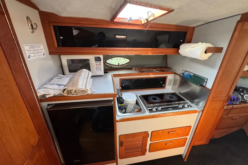 Slide: The Image of 1986 Tiara Yachts 3100 Open galley with stove, microwave, and wooden cabinetry. - 12