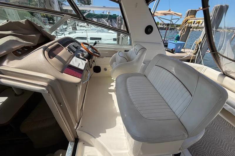 Slide: The Image of 1999 Sea Ray Sundancer 310 cockpit with beige seating and steering wheel, docked at marina. - 14