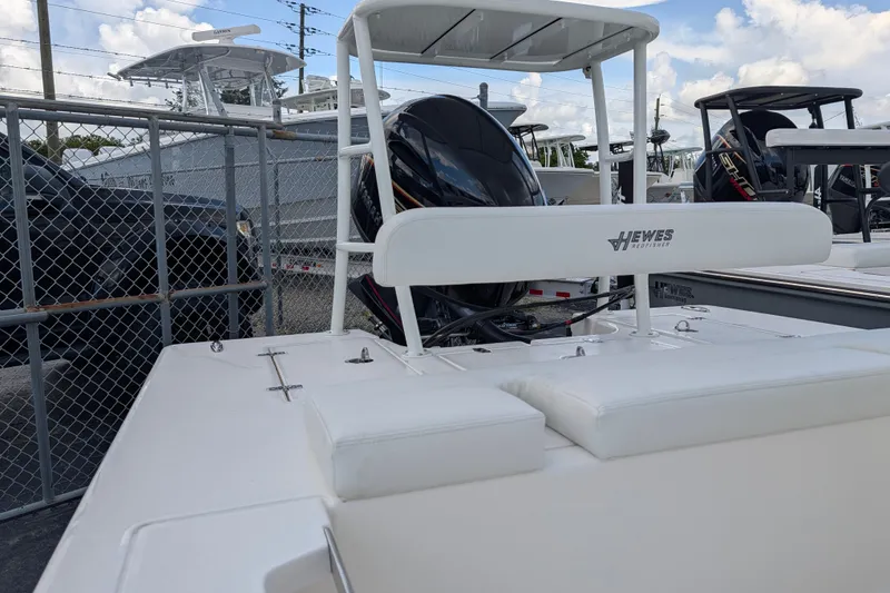 Slide: The Image of A 2027 Hewes Redfisher 16 boat with white upholstery and an outboard motor, parked next to a fence. - 17