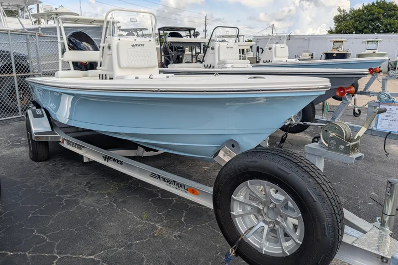 The Image of A light blue boat on a trailer, featuring a white console and an outboard motor. - 0