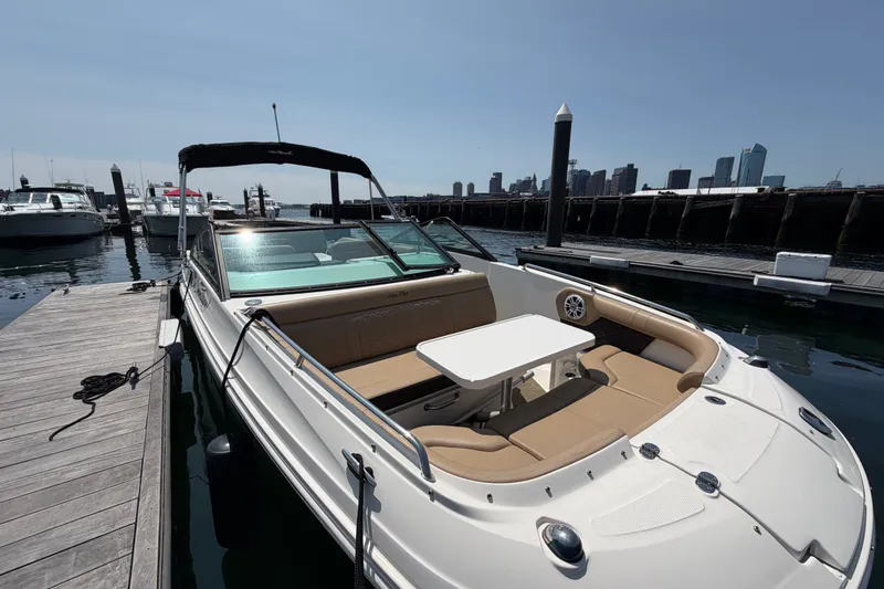 Slide: The Image of 2019 Sea Ray SDX 250 Outboard docked, featuring spacious seating and table, with city skyline backdrop. - 15