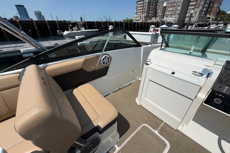 Slide: The Image of 2019 Sea Ray SDX 250 Outboard interior with tan seating and modern dashboard at a marina. - 14