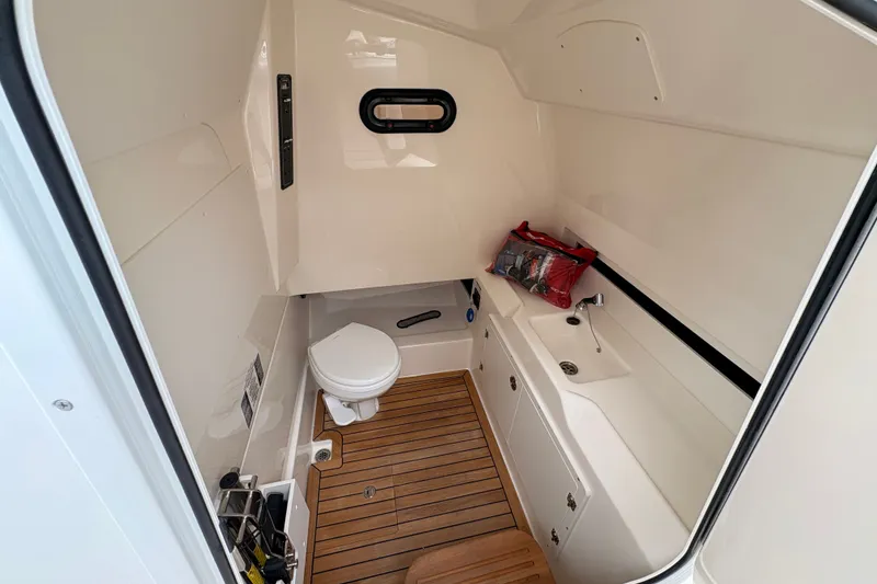 Slide: The Image of 2026 Boston Whaler 330 Outrage cabin interior with toilet and sink, featuring wooden flooring. - 14
