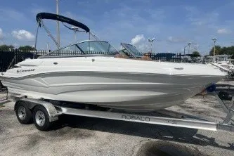 Slide: The Image of 2023 Crownline Eclipse E215 XS boat on trailer, parked outdoors under blue sky. - 2
