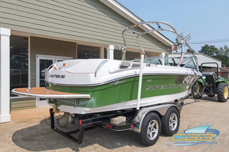 Slide: The Image of 2008 Nautique Super Air Nautique 210 boat on trailer, green and white, parked outside a building. - 28