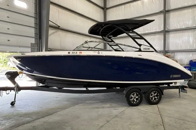 The Image of 2021 Yamaha Boats 252SE in a garage, featuring sleek design and dual-axle trailer. - 0