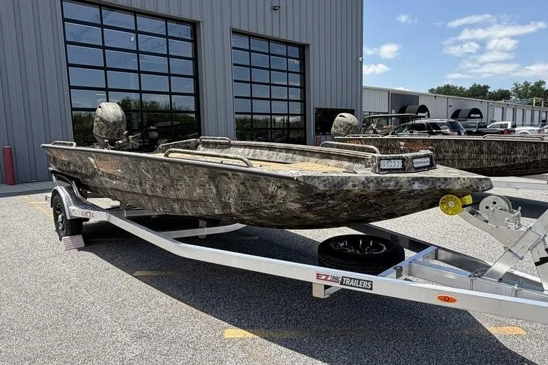 Slide: The Image of 2027 Excel 183 Tomahawk boat on trailer, parked outside industrial building. - 1
