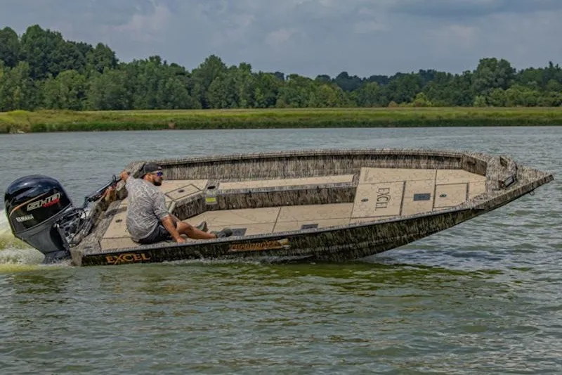 The Image of Man driving 2027 Excel 183 Tomahawk boat on a lake, surrounded by lush greenery. - 2