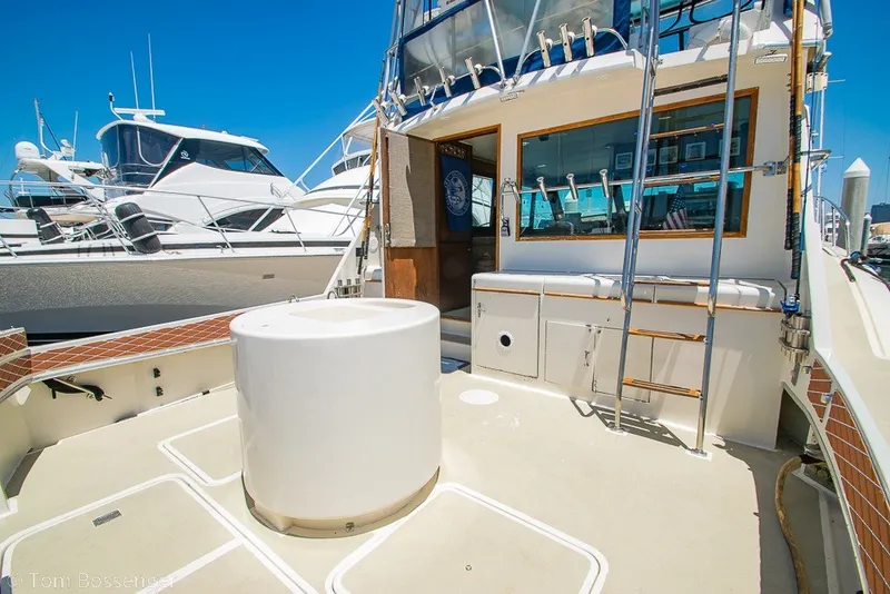 Slide: The Image of 1987 Hatteras 52 Convertible yacht deck with ladder and seating, docked under clear blue sky. - 36