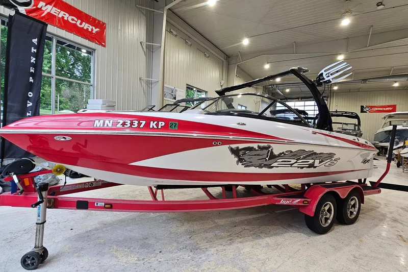 The Image of 2010 Tigé 22Ve boat in showroom, red and white design, on a matching trailer. - 1