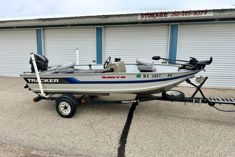 The Image of 1994 Tracker Guide V-14 Riveted Deep V boat on trailer, parked near storage units. - 0