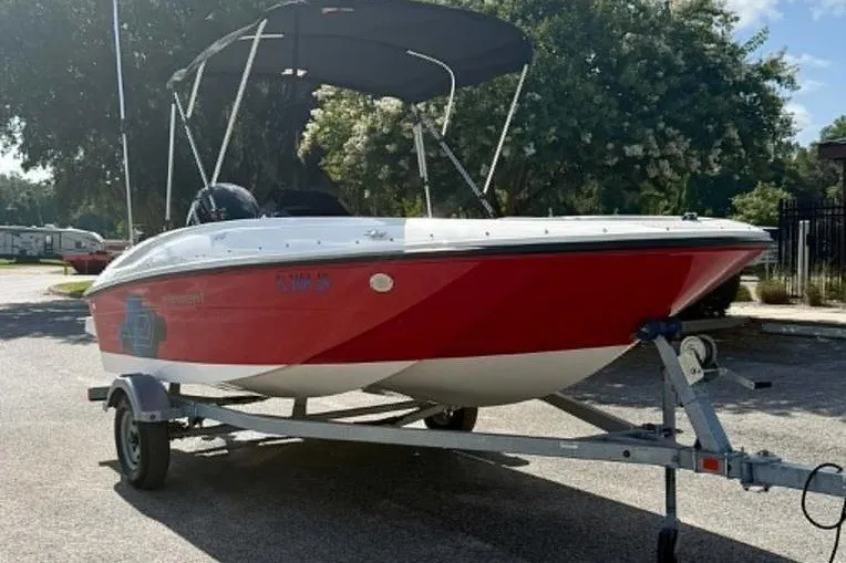 Slide: The Image of 2021 Bayliner Element E16 boat with red hull on a trailer, parked outdoors. - 3