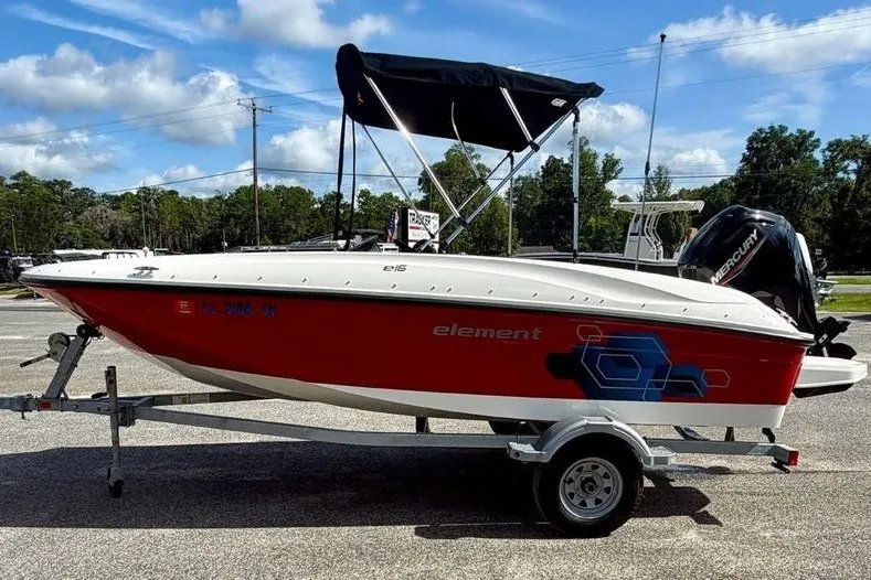 The Image of 2021 Bayliner Element E16 boat on trailer, red hull, black canopy, parked outdoors. - 0
