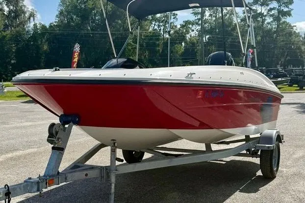Slide: The Image of 2021 Bayliner Element E16 boat with red hull on a trailer, parked outdoors. - 1