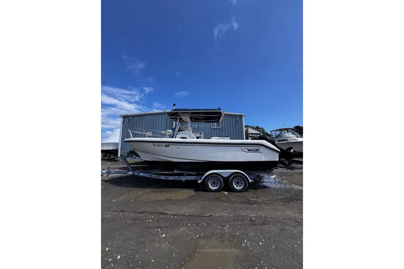 The Image of 2001 Boston Whaler 23 Outrage boat on trailer, parked outdoors under clear blue sky. - 0