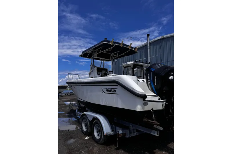 Slide: The Image of 2001 Boston Whaler 23 Outrage boat on trailer, parked outdoors under blue sky. - 2