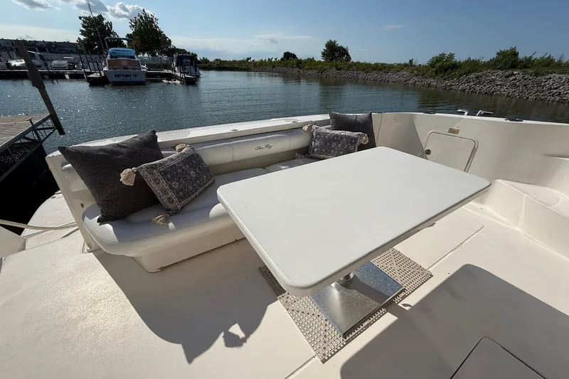 Slide: The Image of 2002 Sea Ray 560 Sedan Bridge yacht deck with seating and table, docked by the water. - 14
