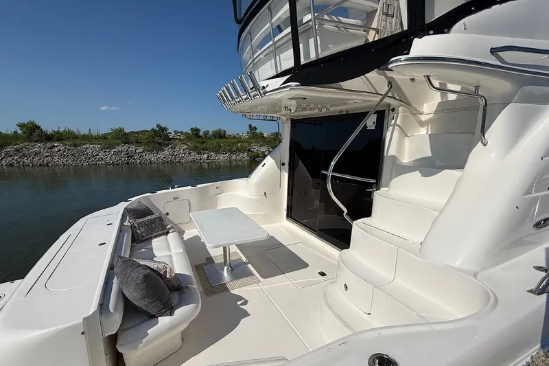 Slide: The Image of 2002 Sea Ray 560 Sedan Bridge yacht deck with seating, table, and scenic water view. - 19