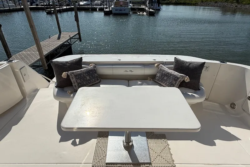 Slide: The Image of 2002 Sea Ray 560 Sedan Bridge yacht deck with seating and table, docked at marina. - 13