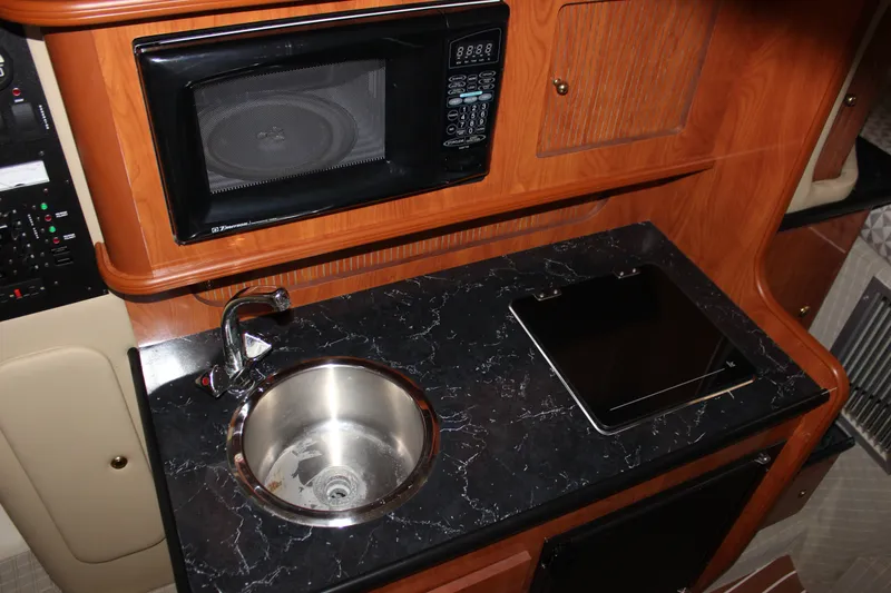 Slide: The Image of 2006 Rinker 290 Express Cruiser kitchen with microwave, sink, and black countertop. - 17