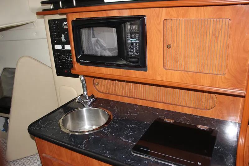Slide: The Image of 2006 Rinker 290 Express Cruiser kitchenette with microwave, sink, and wooden cabinetry. - 28