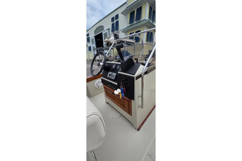 Slide: The Image of 1986 Boston Whaler Outrage 20 boat console with steering wheel and controls, docked near a building. - 13