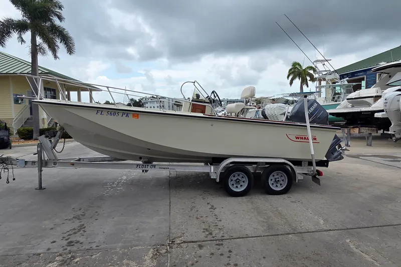 The Image of 1986 Boston Whaler Outrage 20 boat on trailer, parked outdoors under cloudy sky. - 0