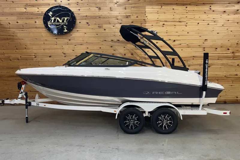 The Image of 2025 Regal 2000 ES boat on trailer, displayed indoors with wooden wall background. - 1