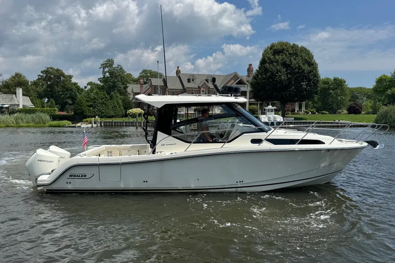 Slide: The Image of 2023 Boston Whaler 325 Conquest boat cruising on a scenic river near luxury homes. - 1