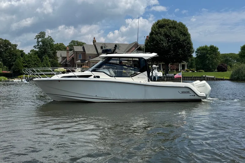 Slide: The Image of 2023 Boston Whaler 325 Conquest boat on a scenic waterway with houses and trees. - 4