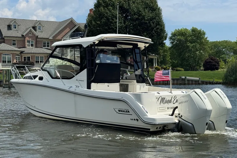 Slide: The Image of 2023 Boston Whaler 325 Conquest boat cruising on a scenic waterway near a large house. - 2