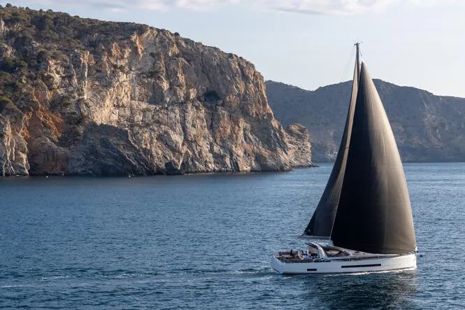 Slide: The Image of Manufacturer Provided Image: Sailing yacht Jeanneau 55 (2026) cruising near rocky coastline under clear skies. - 1