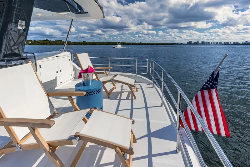 Slide: The Image of Luxurious 2023 Sirena Flybridge yacht deck with chairs, table, and American flag on open water. - 25