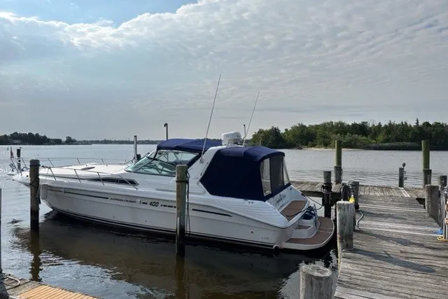 The Image of 1992 Sea Ray 400 Express Cruiser docked by a serene waterfront under a cloudy sky. - 0