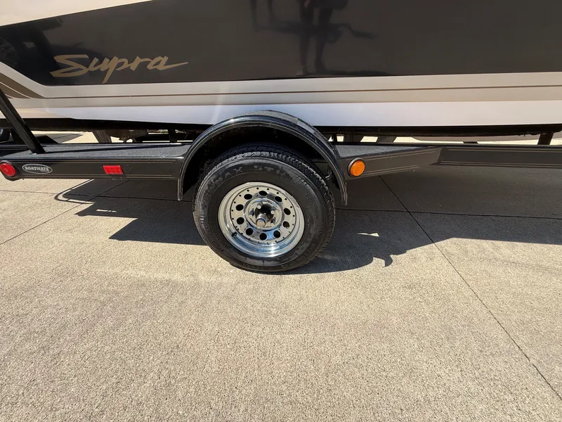 Slide: The Image of A 1999 Supra boat on a trailer, featuring a shiny wheel and a black stripe. - 18