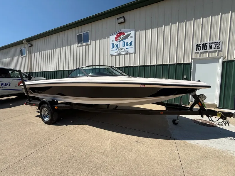 Slide: The Image of A white and black boat on a trailer in front of a building with a "Boji Boat" sign. - 1