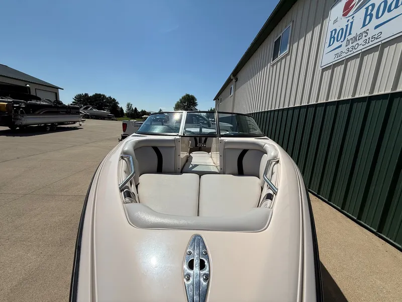 Slide: The Image of A 1999 Supra Legacy boat with beige interior, parked on a concrete lot next to a building. - 3