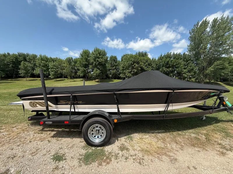 Slide: The Image of A 1999 Supra Legacy boat on a trailer, covered with a black tarp, set on grassy terrain. - 19
