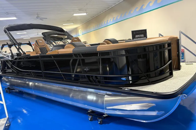 The Image of 2027 South Bay 525UL pontoon boat with sleek black design and tan seating in showroom. - 0