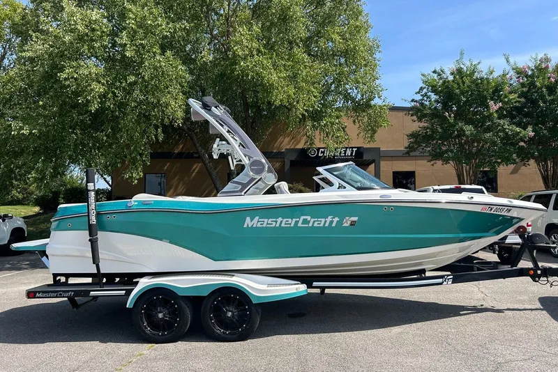 The Image of 2017 MasterCraft XT23 boat on trailer, teal and white, parked outdoors. - 0
