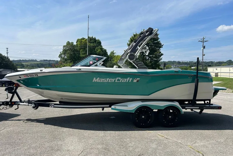 Slide: The Image of 2017 MasterCraft XT23 boat on trailer, teal and white design, parked outdoors. - 3
