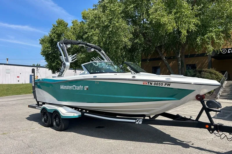 Slide: The Image of 2017 MasterCraft XT23 boat on trailer, teal and white, parked outdoors under clear sky. - 1